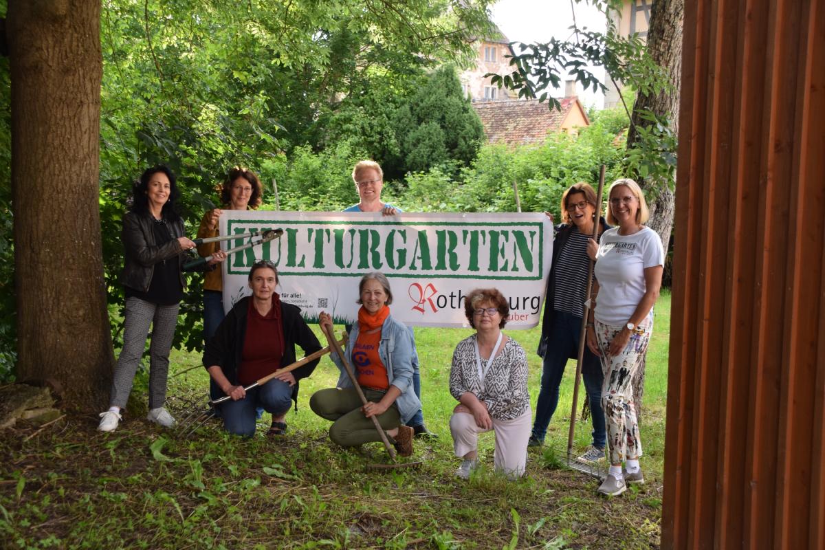 Eine Gruppe vom Menschen steht in einem Garten und hält ein Banner mit der Aufschrift "Kulturgarten" hoch