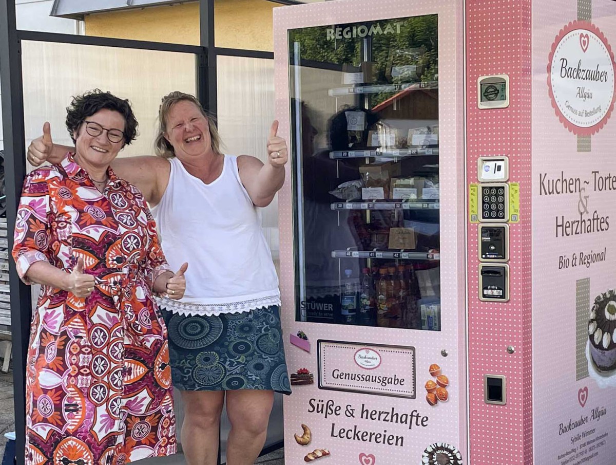 Sybille Wimmer von "Backzauber Allgäu" und Heimatentwicklerin Manuela Müller-Gaßner freuen sich über die Inbetriebnahme des Kuchen-Verkaufsautomaten.