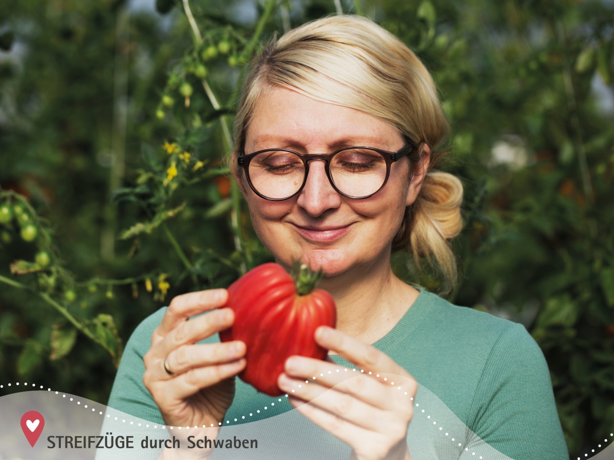 Eine junge Unternehmerin betrachtet eine Tomate, sie lächelt