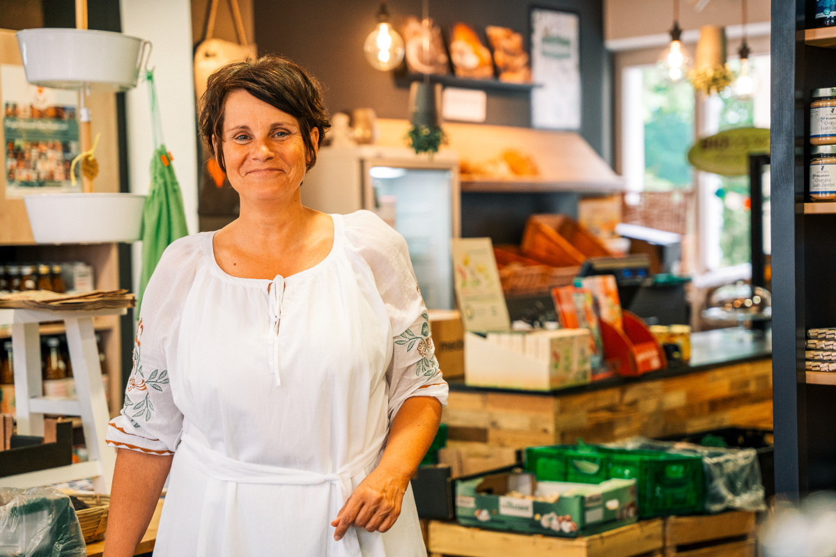 Eine Frau steht in einem kleinen Laden und lächelt freundlich in die Kamera