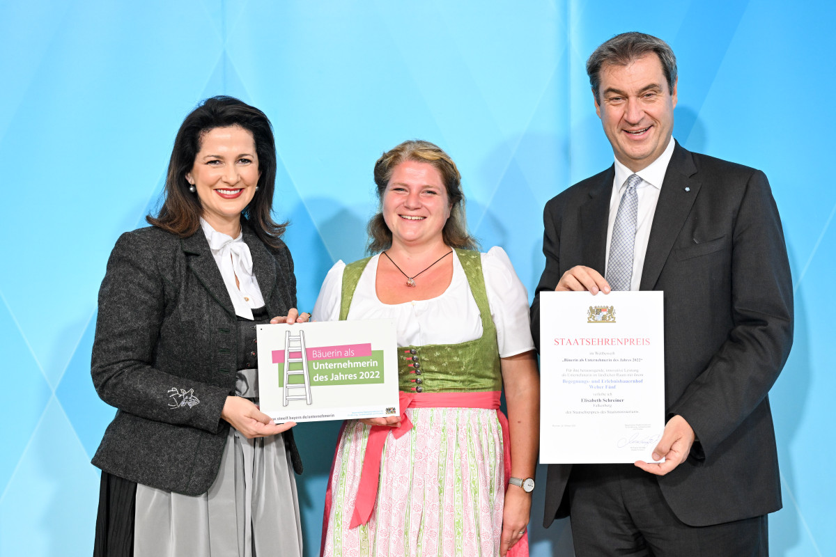 Eine junge Frau steht strahlend mit einer Urkunde in der Hand zwischen zwei Politikern