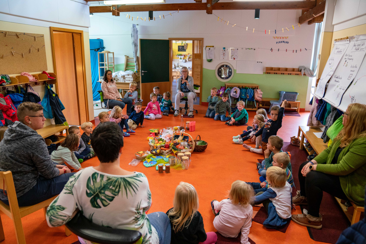 Kinder sitzen im Kreis mit Lebensmitteln und Behältern in der Mitte.