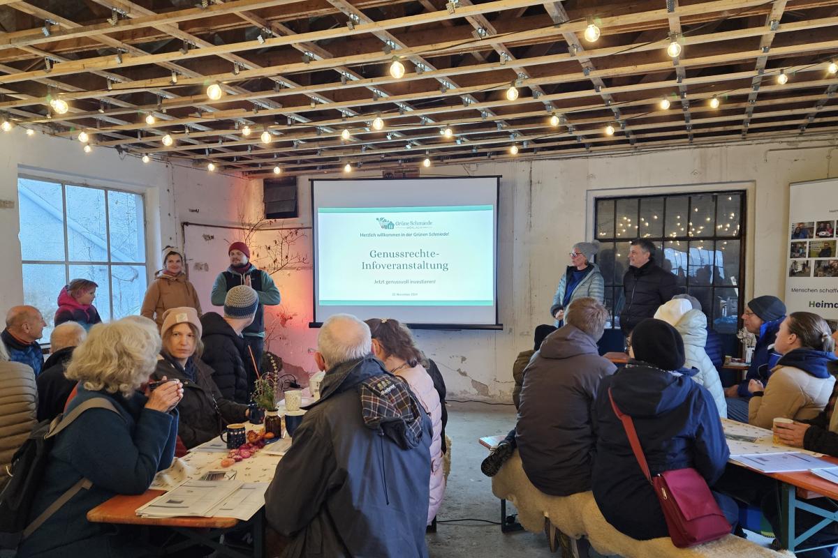 Menschen sitzen an Biertischen und hören einer Präsentation zu