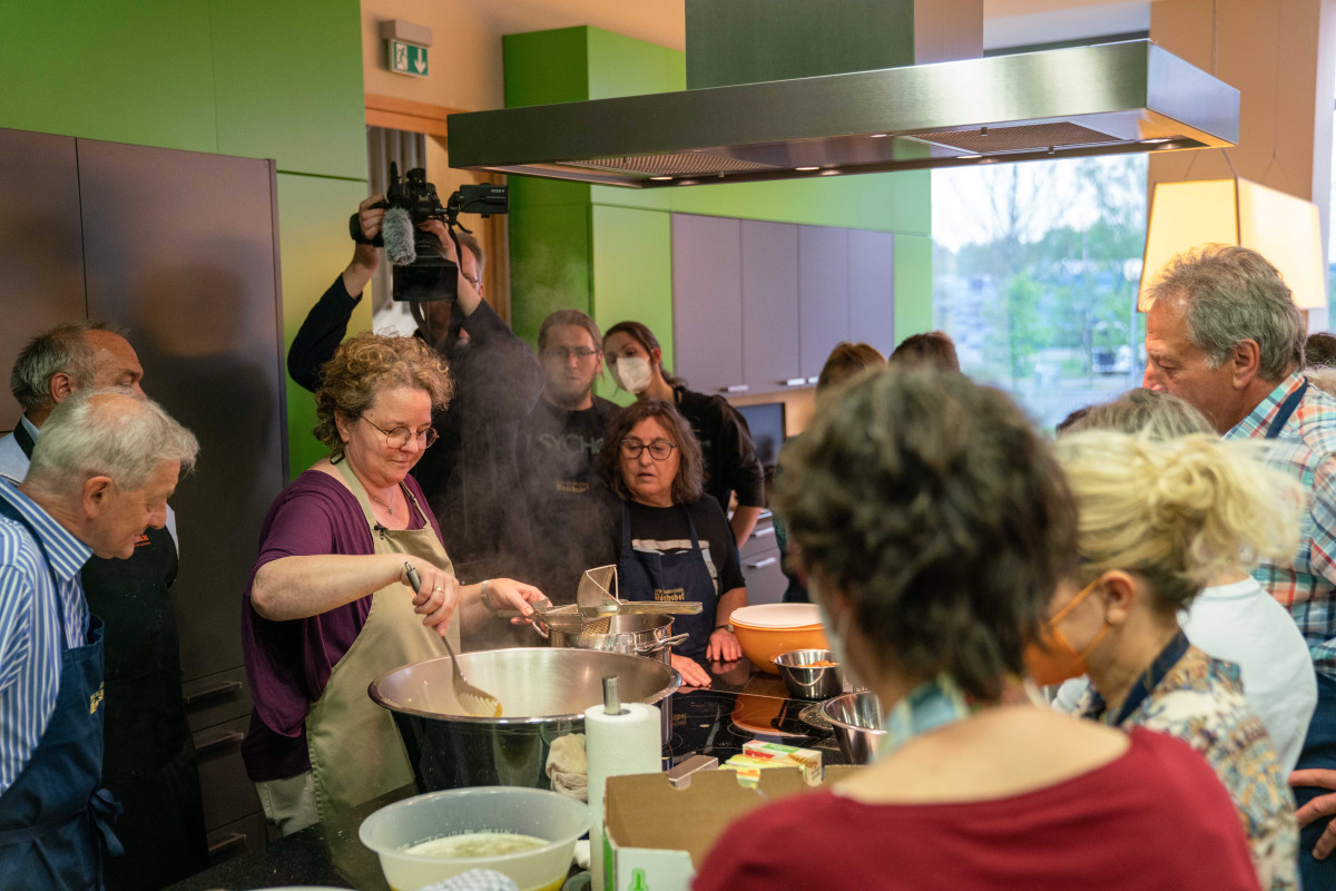 Kerstin Rentsch steht vor dem Kochtopf, die Teilnehmer um sie herum
