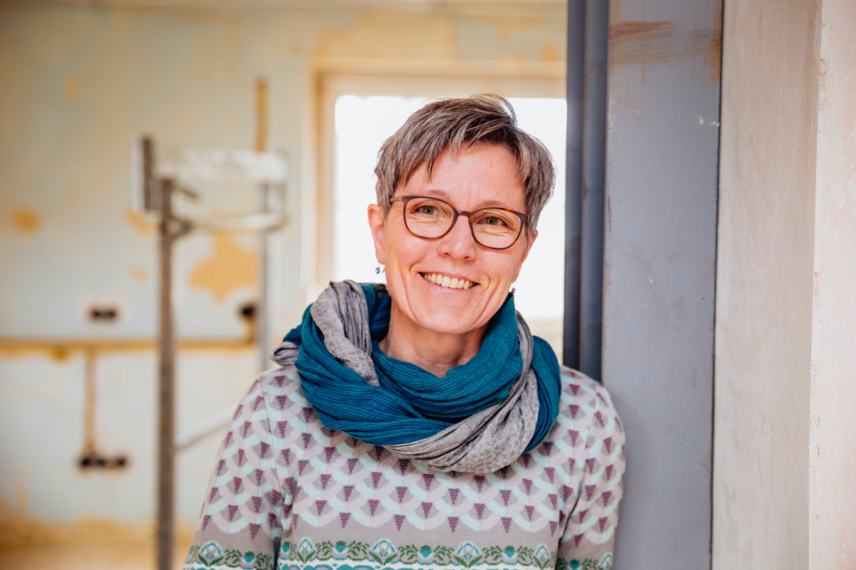 Eine Frau mit grauen Haaren, Brille und Schal lächelt in die Kamera.