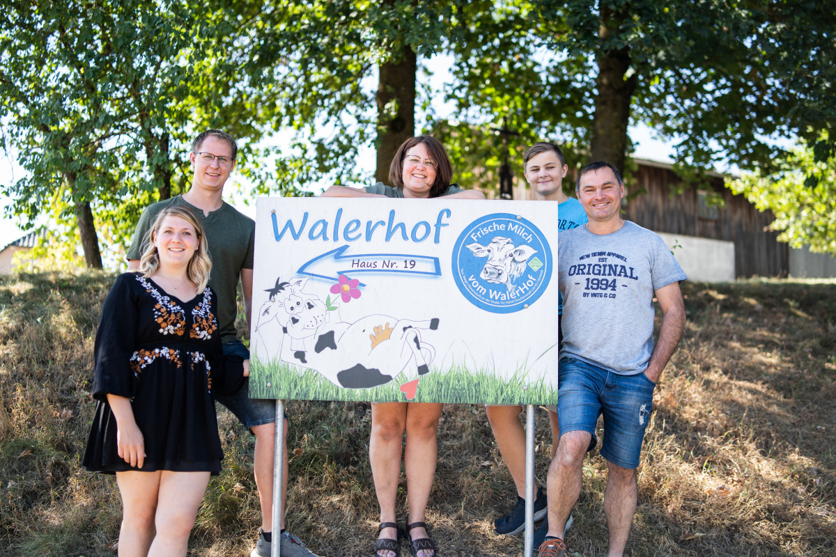 Fünfköpfige Familie steht um das "Walerhof"-Schild in der Natur