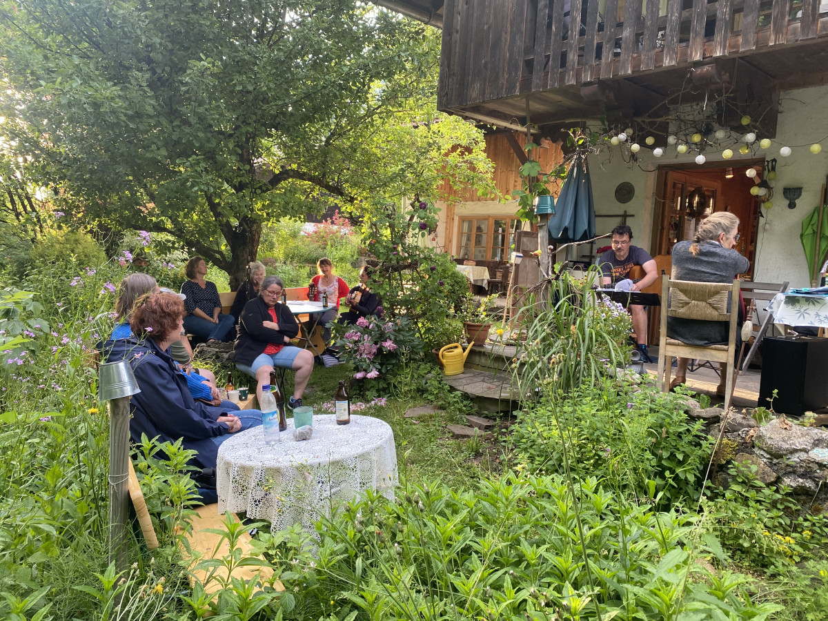 Zwei Frauen singen und spielen Gitarre in einem Garten, Zuschauer drumherum