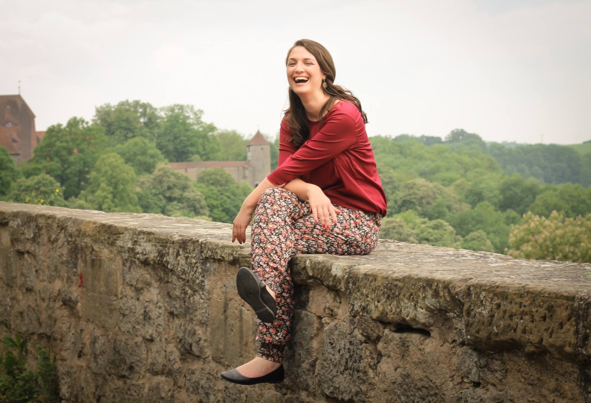 Eine Frau sitzt lachend auf einer Mauer