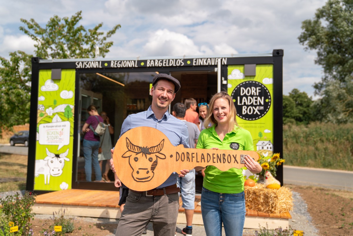 Julius Stintzing und Jana Bumann-Rid halten symbolischen Schlüssel bei der Eröffnung der Dorfladenbox.