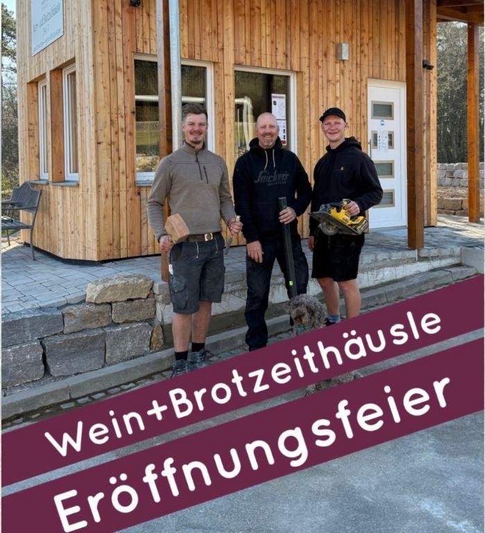 Drei Männer stehen vor einem kleinem Holzhäuschen