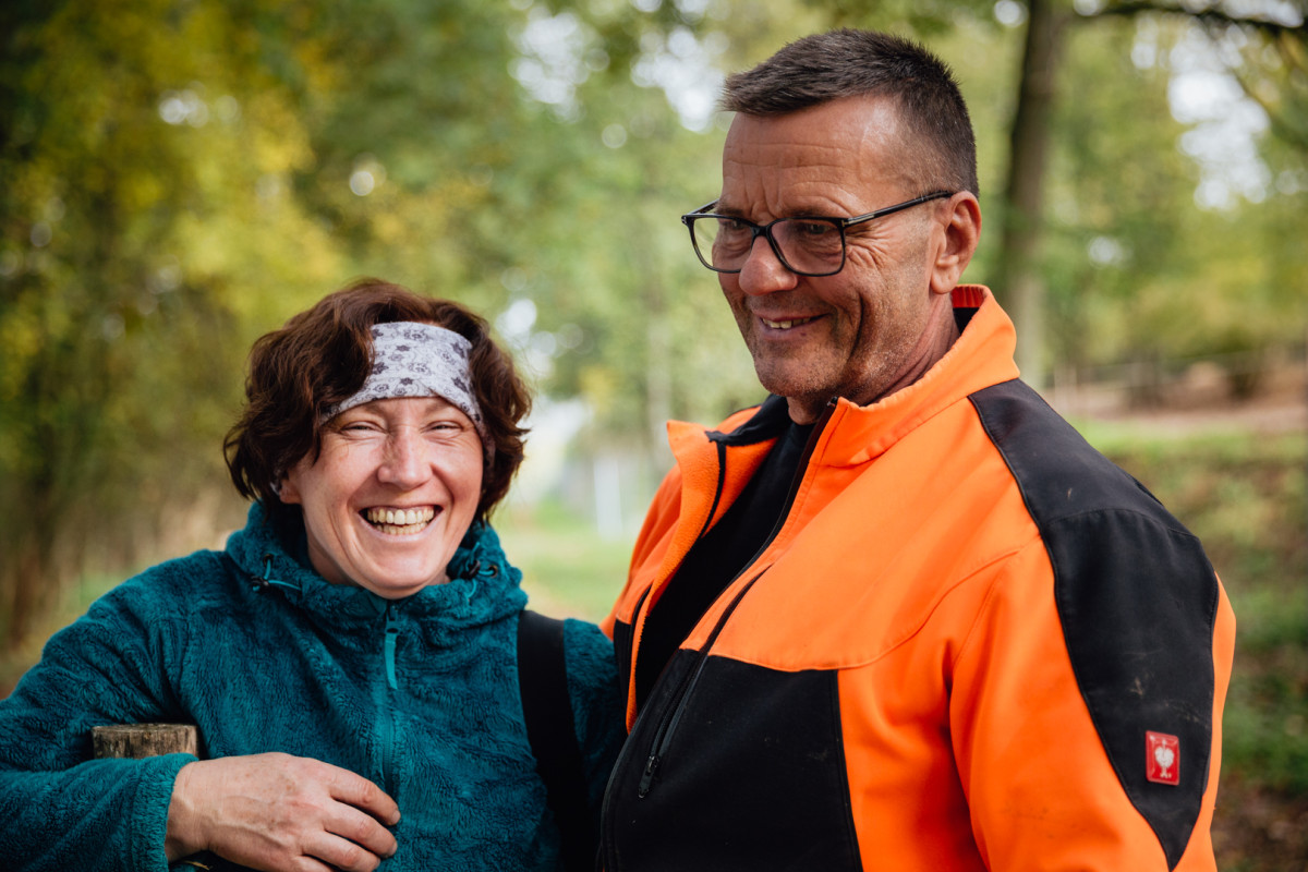 Eine Frau und ein Mann lächelnd. Im Hintergrund ist Wald zu sehen.